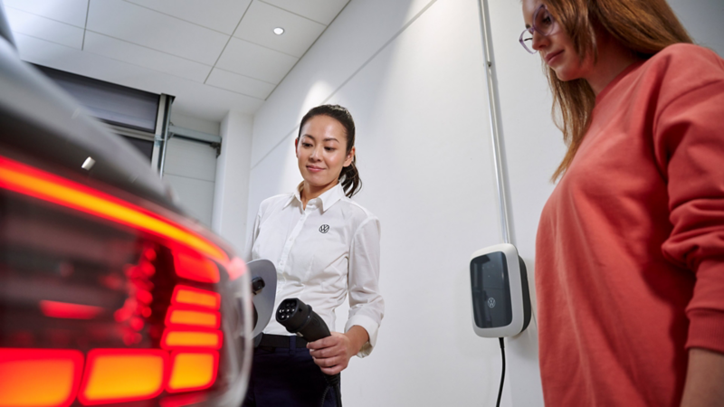 Eine VW Servicemitarbeiterin erklärt einer Frau das Laden an einer Wallbox beim VW Service.