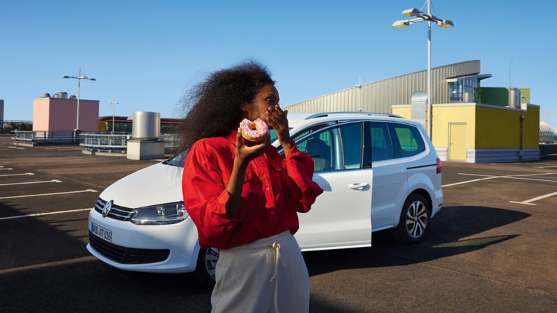 Weißer VW Sharan ACTIVE steht mit geöffneter Tür auf einem urbanen Parkplatz. Frau mit rotem Hemd davor.