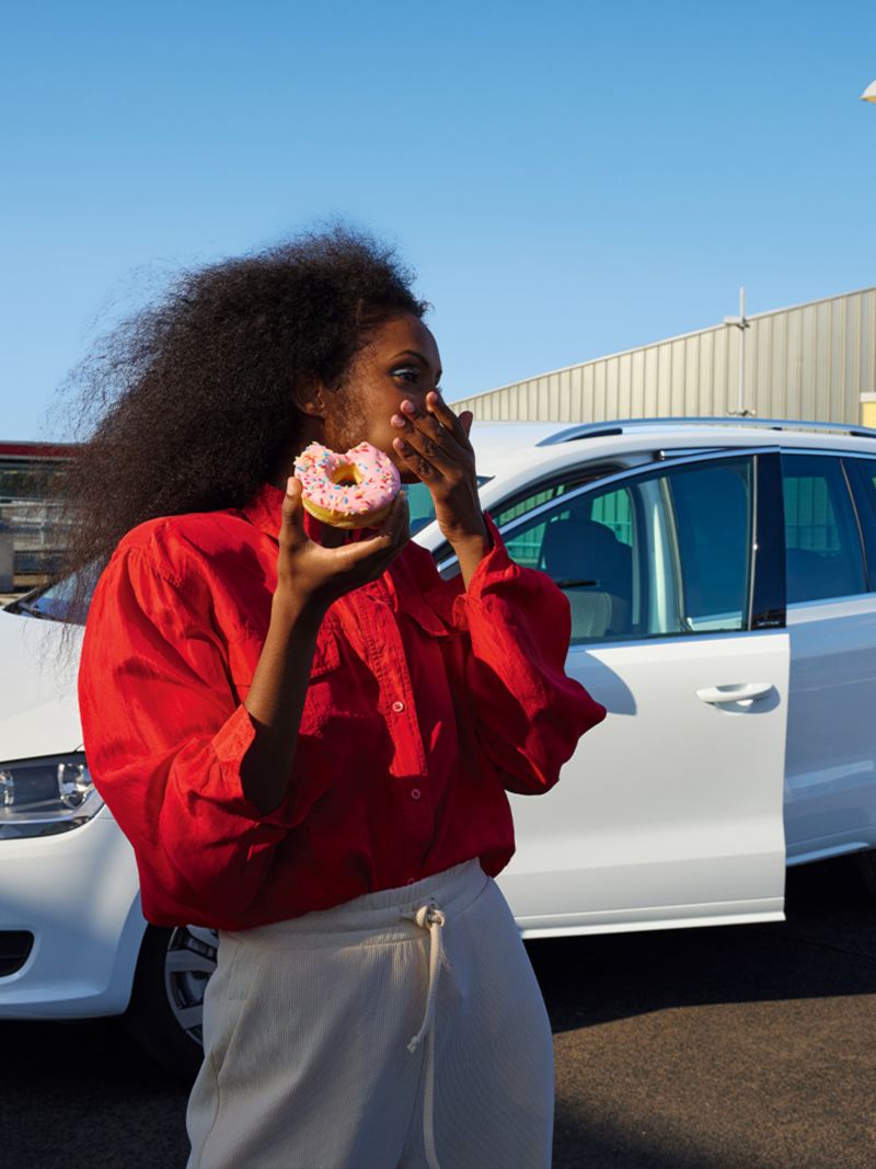 Weißer VW Sharan ACTIVE steht mit geöffneter Tür auf einem urbanen Parkplatz. Frau mit rotem Hemd davor.
