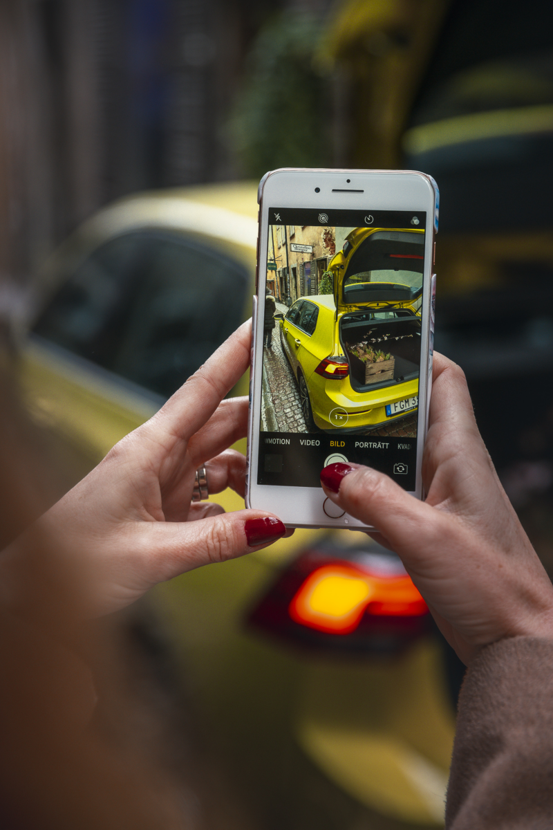 En person tar ett foto med en iPhone på en gul Volkswagen med en blombukett i bagageutrymmet