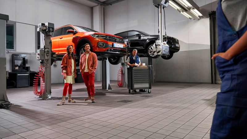 Two customers and a VW service employee in the workshop, VW T-Cross and VW Touareg on lifting platforms