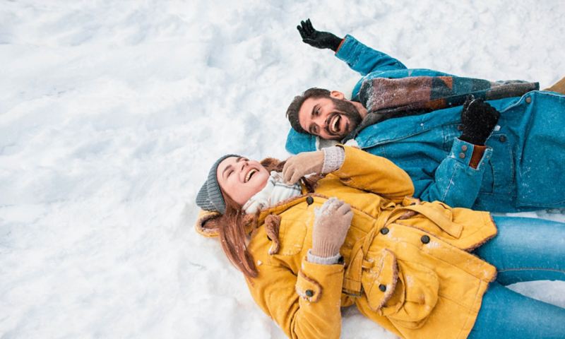 Due persone stese sulla neve ridono insieme.