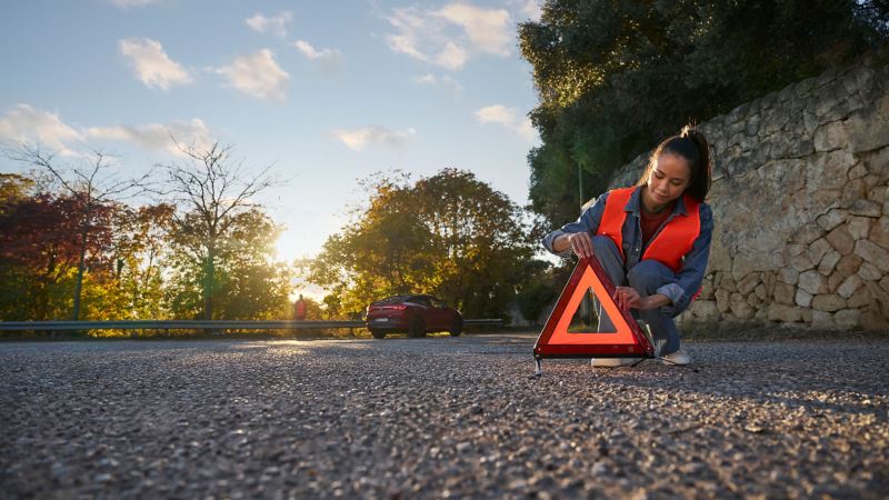 Une femme portant un gilet de sécurité place un triangle d'avertissement, avec une VW ID.5 GTX en arrière-plan