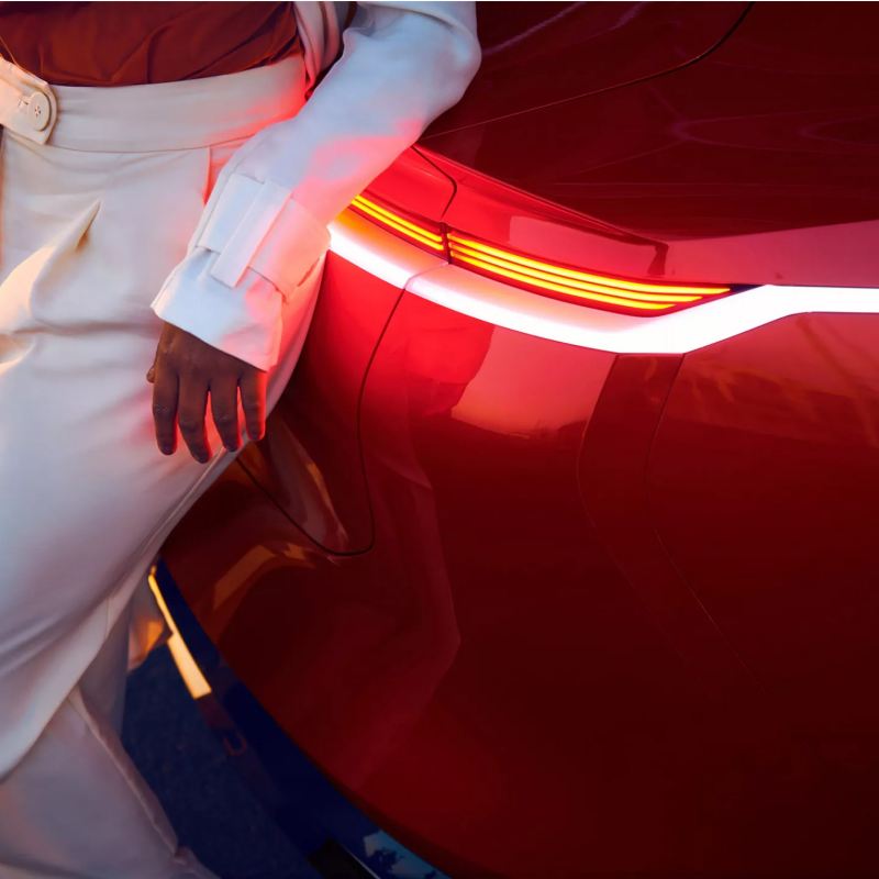 Fashionable woman standing next to red VW electric vehicle.