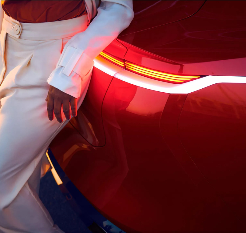 Fashionable woman standing next to red VW electric vehicle.