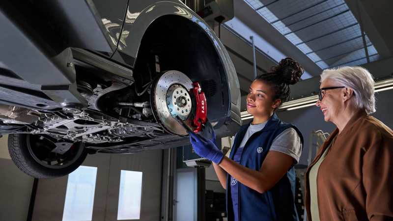 Kobieta mechanik oraz klientka dokonujący inspekcji tarcz hamulcowych w samochodzie na podnośniku