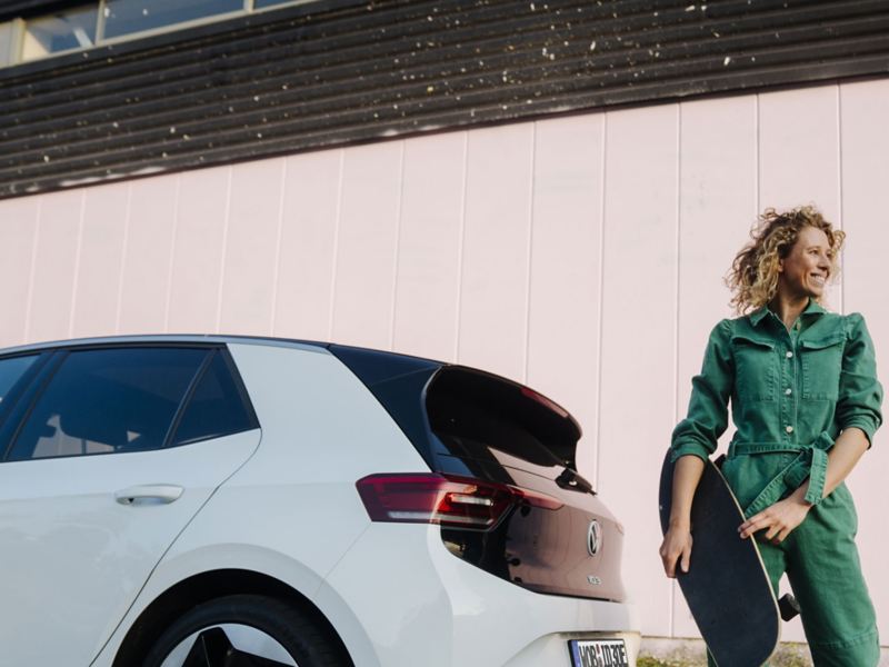 Eine junge Frau steht neben ihrem Elektroauto.