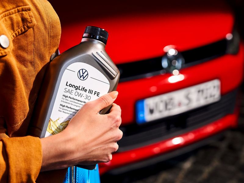 A woman holds an engine oil bottle in her hands in front of a Volkswagen