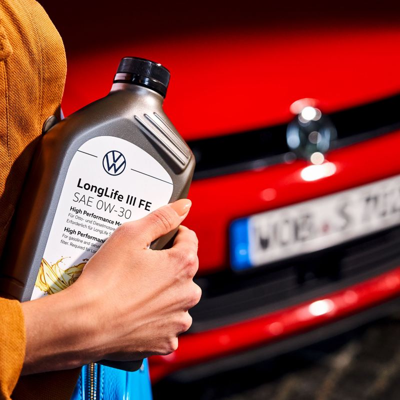 A woman holds an engine oil bottle in her hands in front of a Volkswagen