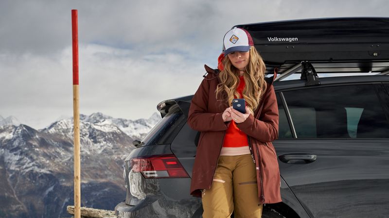 Kvinna med mobil framför en VW med takbox