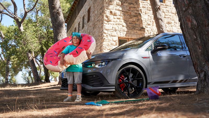 A boy with a donut pool float standing in front of a VW Golf 8 GTI
