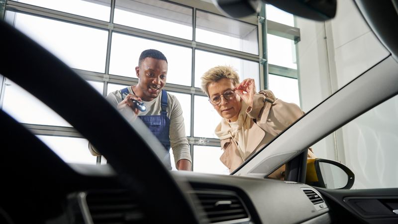 Un collaborateur de service VW et un client examinent un éclat sur un pare-brise.