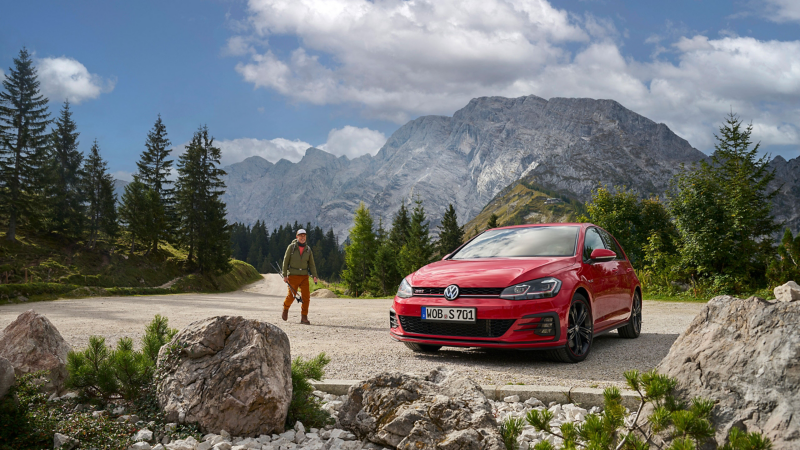 Ένας άντρας δίπλα σε ένα κόκκινο Golf 7- compact car παλαιότερο μοντέλο.