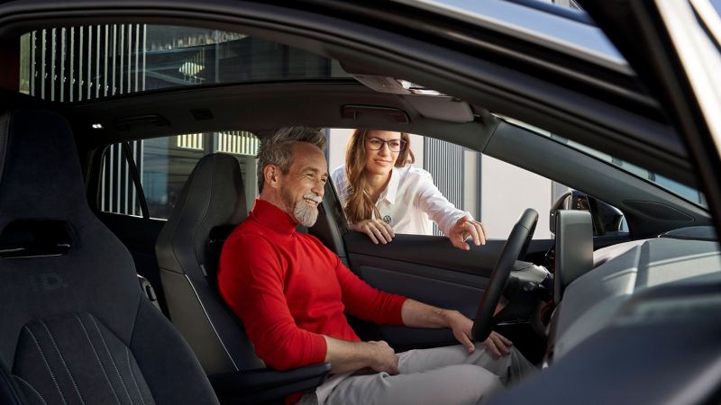 Μια υπάλληλος εξυπηρέτησης πελατών VW δείχνει σε έναν πελάτη τις αναβαθμίσεις στο όχημά του μετά από μία ενημέρωση λογισμικού.