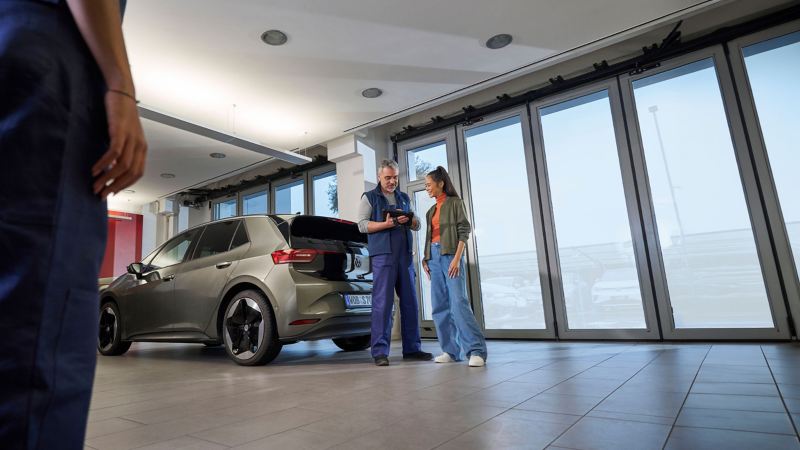 Un addetto all’assistenza Volkswagen e una cliente vicino a una Volkswagen ID.3 guardano un tablet