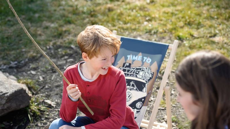 A laughing child with clothes from the Heritage Collection sits on a deck chair – VW Lifestyle products