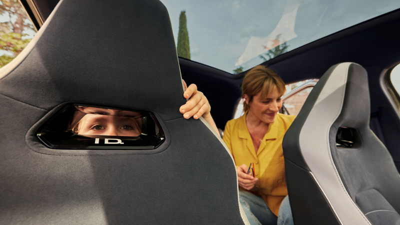 Mutter und Tochter sitzen auf der Rücksitzbank eines ID. Modells, die Tochter schaut durch eine Öffnung am Sitz nach vorn