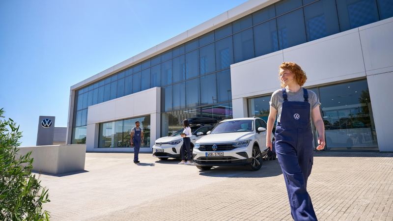 A VW service employee next to two Volkswagen