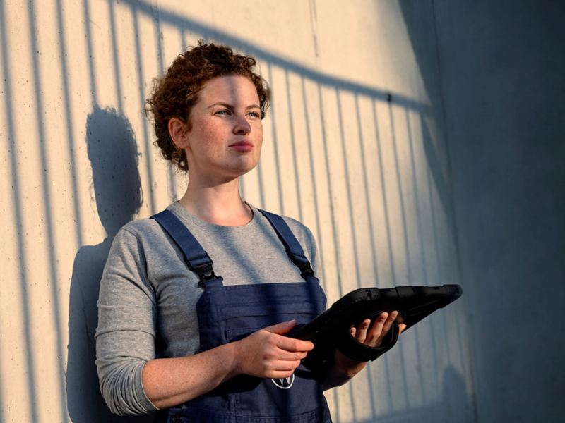 Une collaboratrice du service entretien se tient appuyée contre un mur en tenant une tablette dans sa main