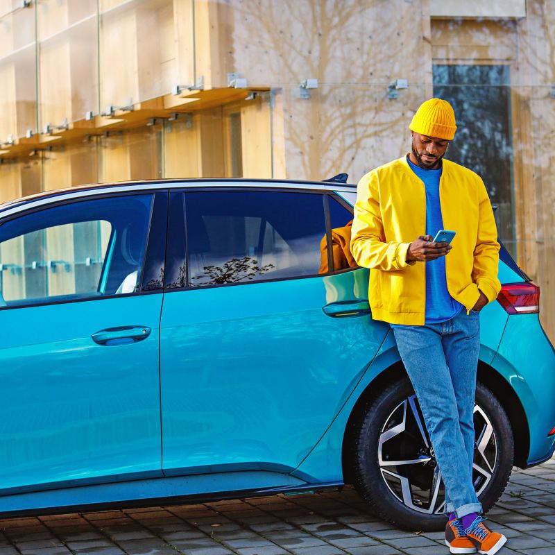 Ein Mann in einer gelben Jacke lehnt an seinem VW ID.