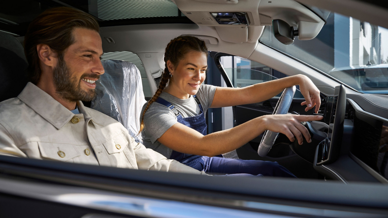 VW Servicemitarbeiterin und Mann sitzen in VW Auto und schauen auf Infotainment-System für Software Updates