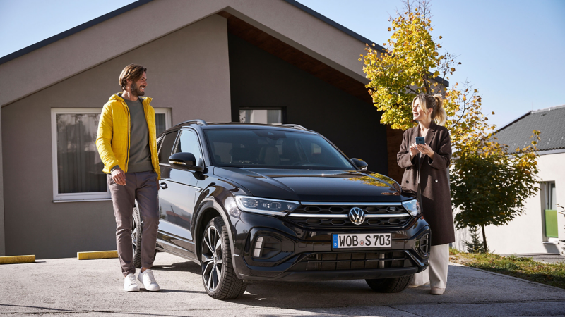 Mujer con un smartphone y un hombre junto a un coche Volkswagen.