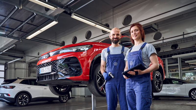 Eine VW Servicemitarbeiterin steht vor einem Volkswagen ID.5 auf einer Hebebühne in einer Werkstatt.