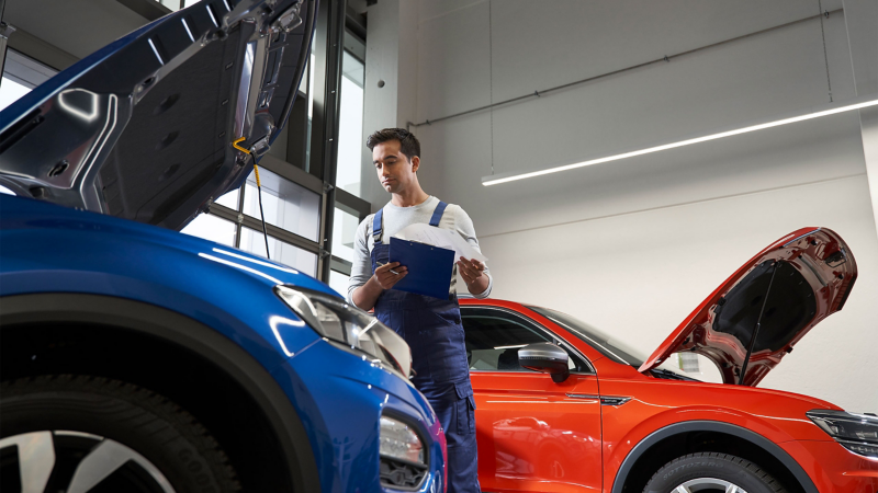 mężczyzna w warsztacie samochodowym przyglądający się silnikowi w niebieskim Volkswagenie