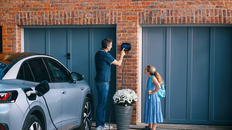 Girl watches man operating the Ohme home charger – VW ID. electric car being charged