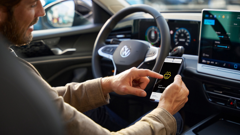 A man sitting in a Volkswagen car checking his phone