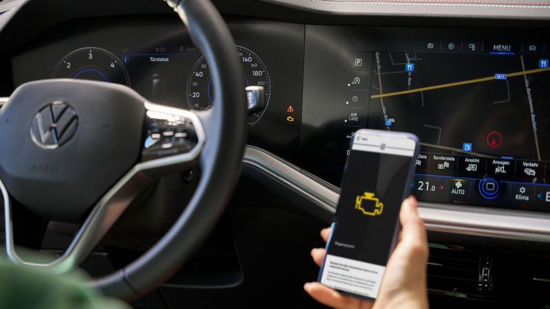 Nahaufnahme VW Cockpit, im Vordergrund ein Smartphone mit Informationen zu einer Warnlampe