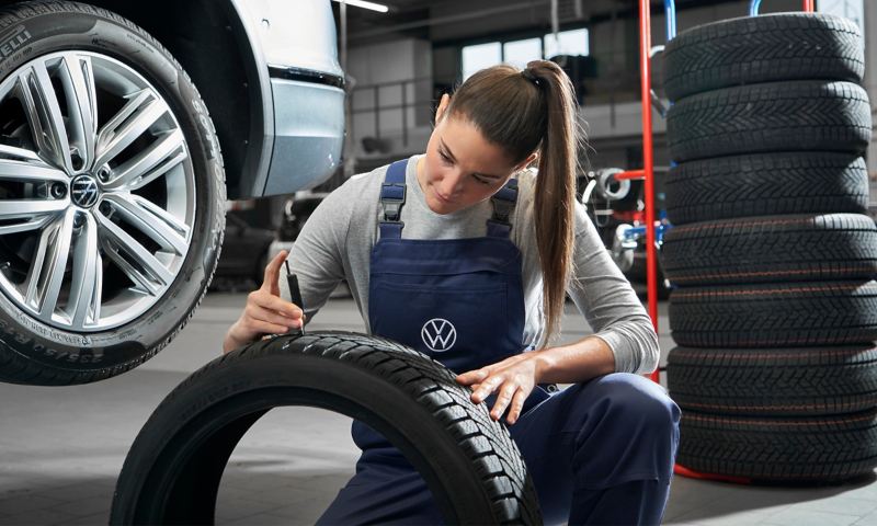 Un collaborateur de service de VW examine le pneu d’une VW rouge – informations sur les roues