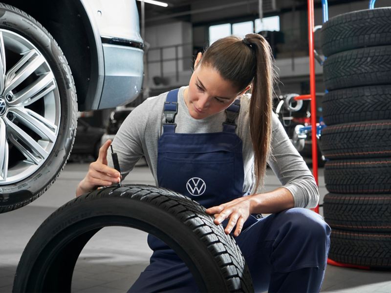 Un collaborateur de service de VW examine le pneu d’une VW rouge – informations sur les roues