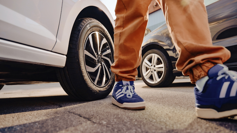 Nahaufnahme von Person mit blauen Turnschuhen vor zwei VW Autos – Räder und Reifen im Fokus