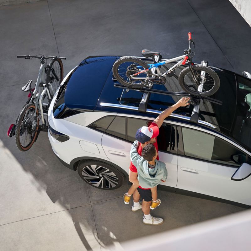 One man is packing their things into their grey VW with a kayak rack and foldable rear bike rack – transport on holiday