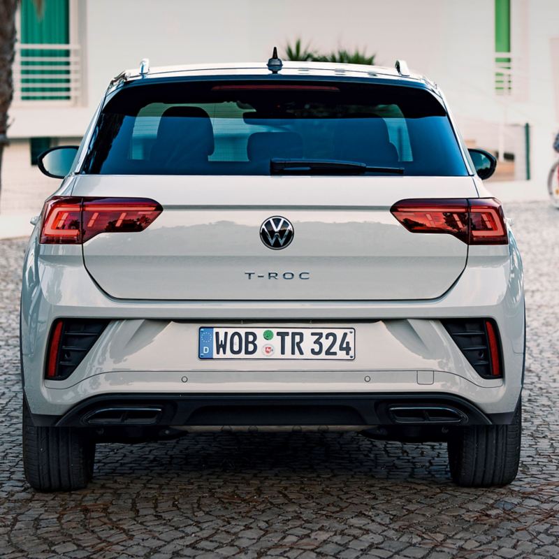 VW T-Roc mit Umbau für Menschen mit Behinderung parkt an einem Haus. Im Hintergrund eine Frau im Rollstuhl.