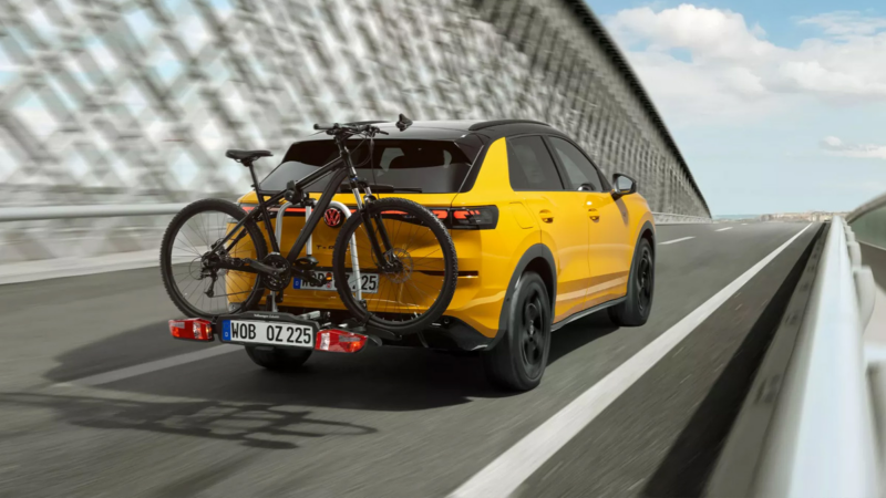 Gele Volkswagen T-Roc rijdt over een brug met een fiets op de fietsendrager.