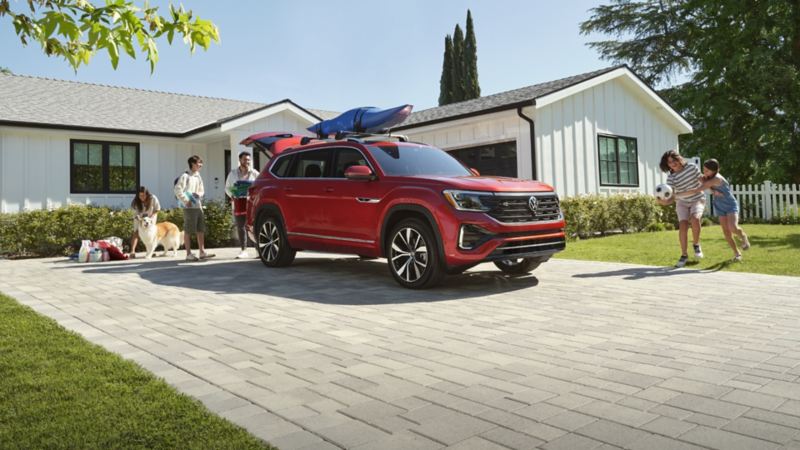 Une famille près d’un Volkswagen Atlas rouge avec un kayak sur le toit