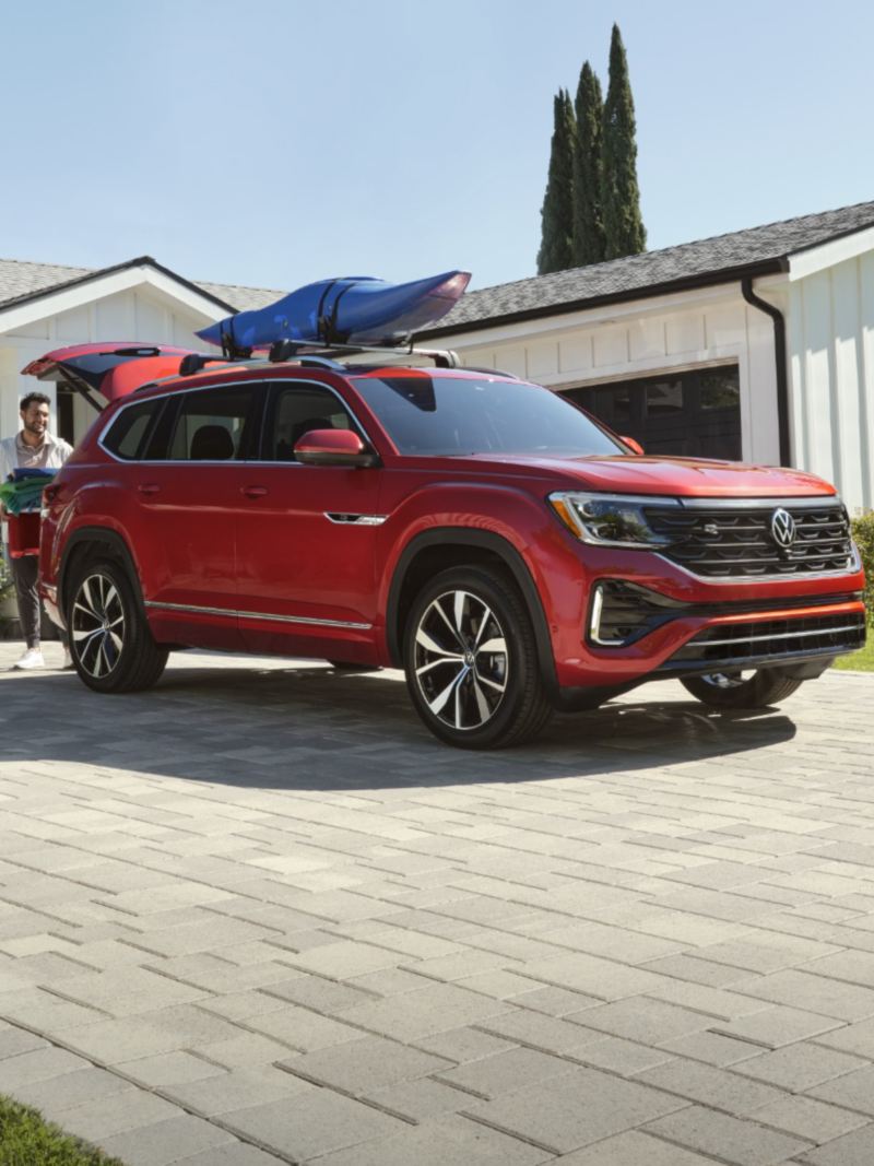 A family near a red Volkswagen Atlas with a kayak on the roof