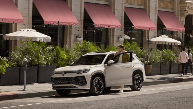 2026 Volkswagen Tiguan SUV in white with a person holding the open driver’s door in an urban setting.