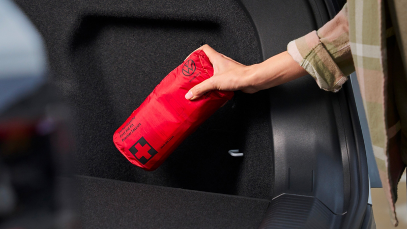 Una persona ripone nel bagagliaio il kit di sicurezza per il soccorso stradale Volkswagen.