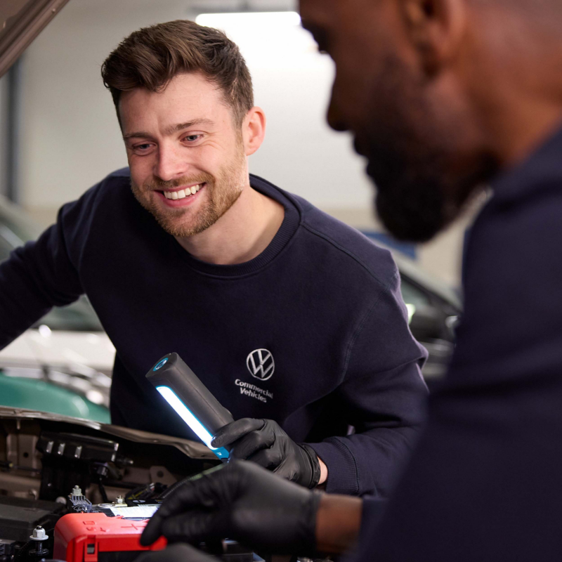 Two VW service technicians looking under the bonnet of a VW Amarok