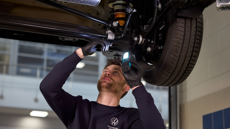 A man wearing overalls and gloves working under a vehicle.