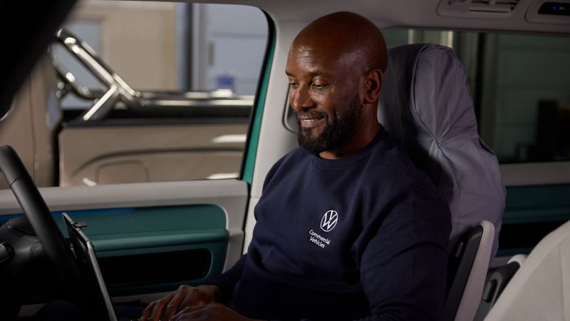 A VW technician using a laptop while sitting in the passenger seat of a VW vehicle. 