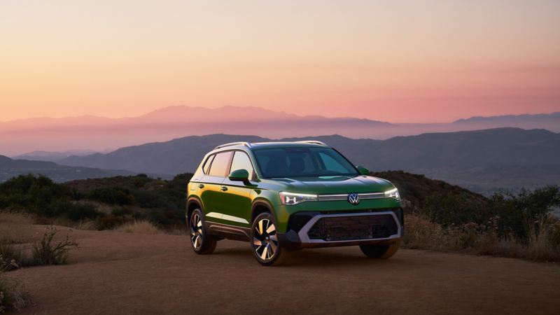 Un plan avant trois/quarts d’un Taos 2025 vert Serrano au coucher du soleil, stationné sur une montagne.