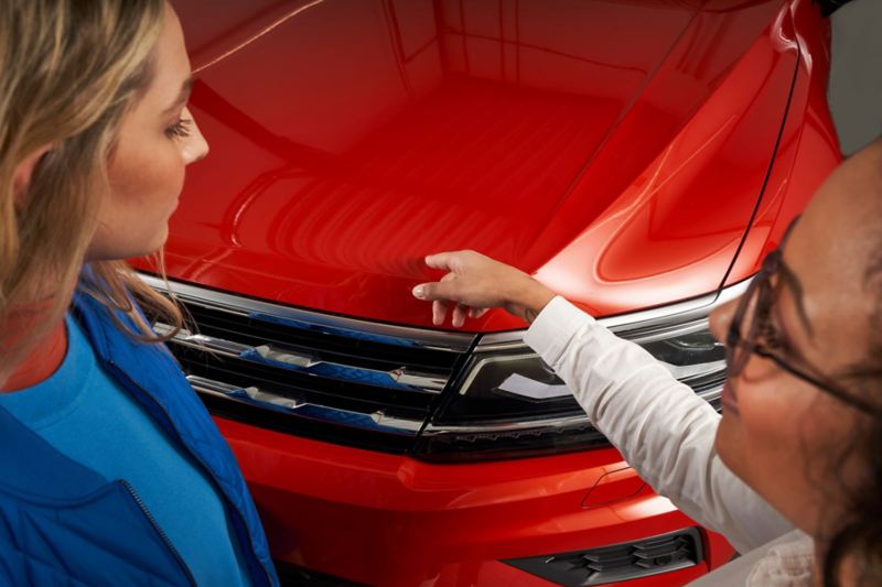 Une technicienne du service entretien et une cliente inspectent la carrosserie d'une Volkswagen