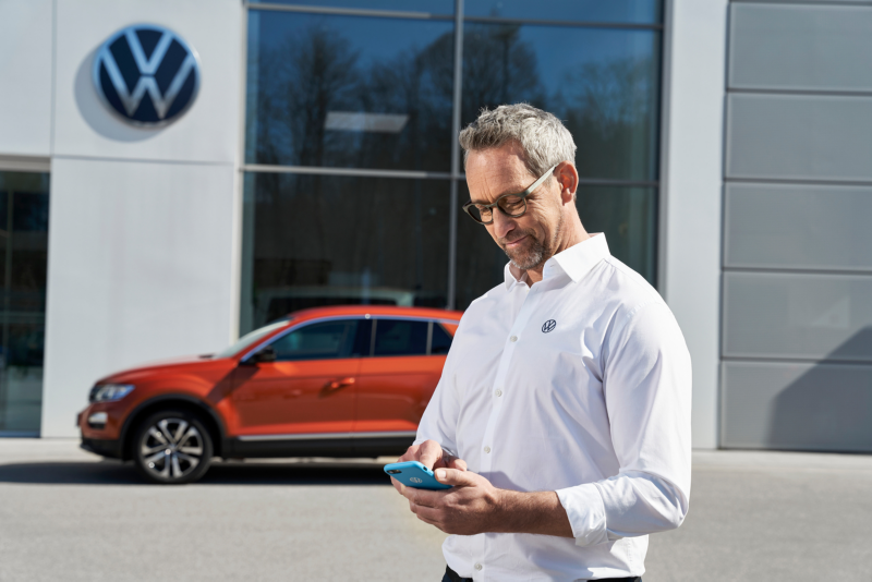 En Volkswagen medarbejder står med en telefon i hånden foran en forhandler