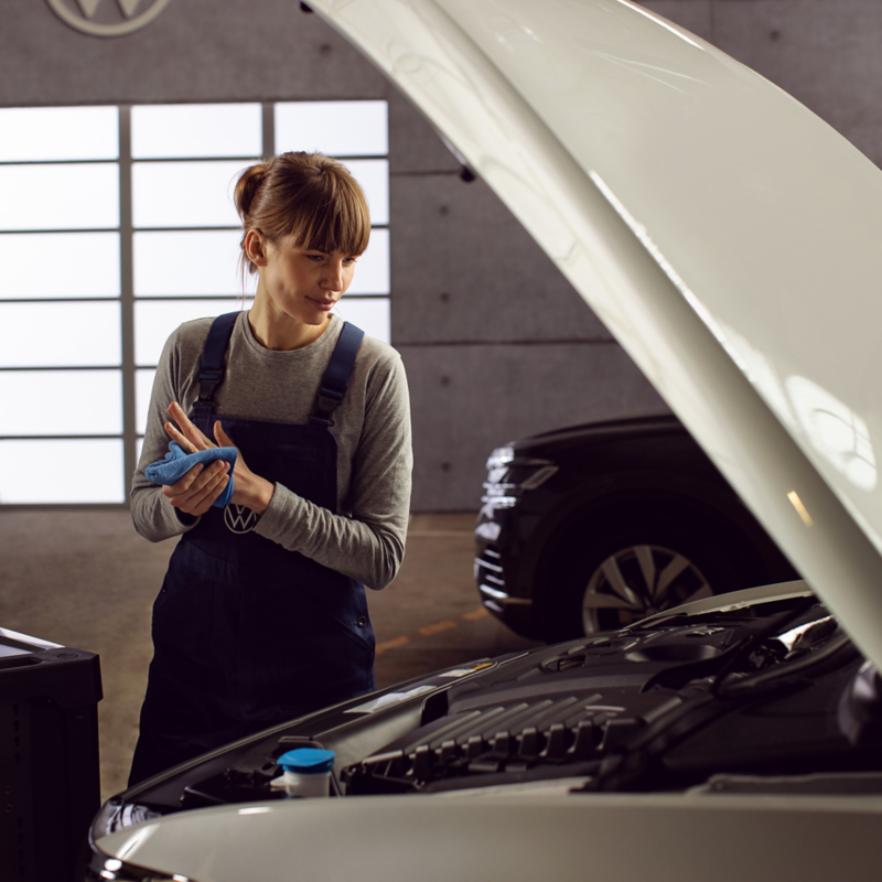 Servicekvinna i VW-verkstad står och tittar ner i en motor