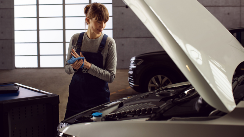 En kvinnlig verkstadsarbetare torkar händerna och tittar ner under motorhuven på en vit Volkswagen