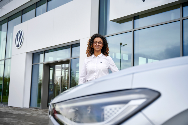 Woman standing in front of a Volkswagen dealership service center.